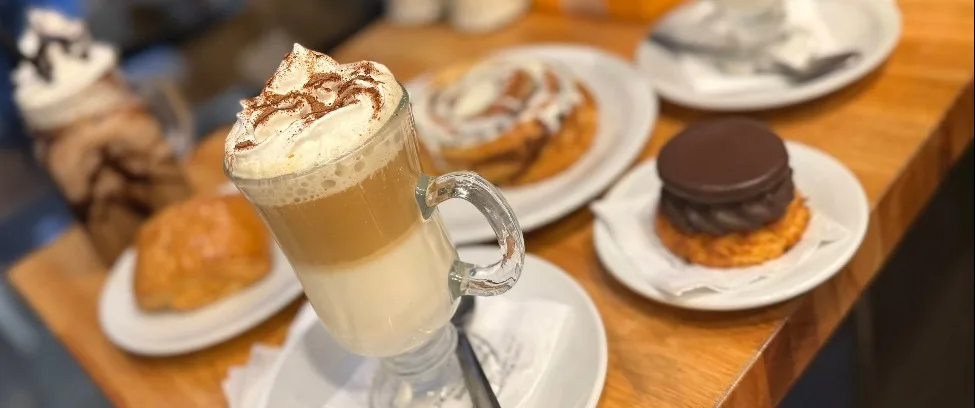 Café con leche cortado con crema y canela, junto a facturas y postres